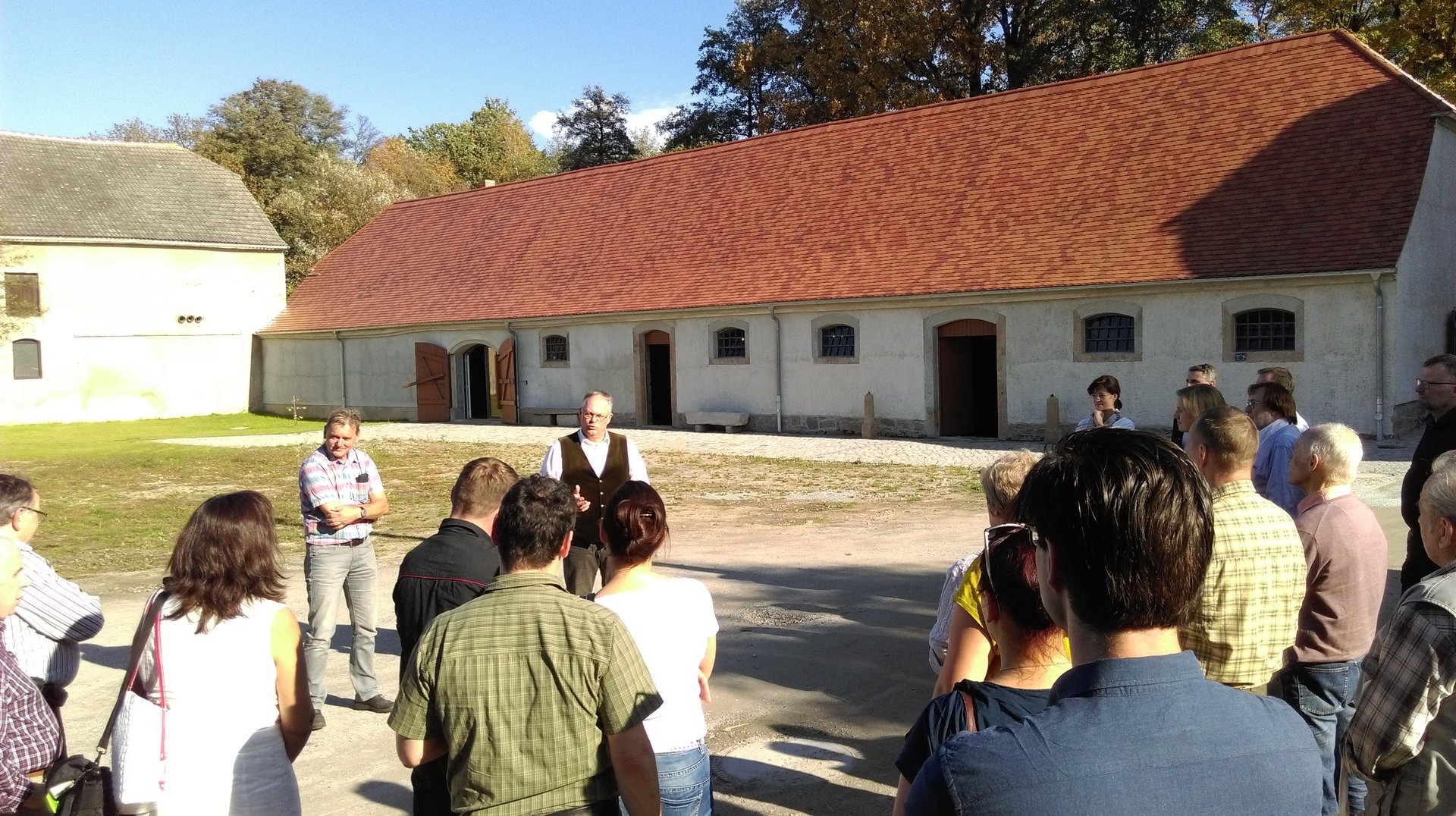 eien Gruppe von Menschen steht im Innenhof eineslandwirtschaftlichen Hofes.