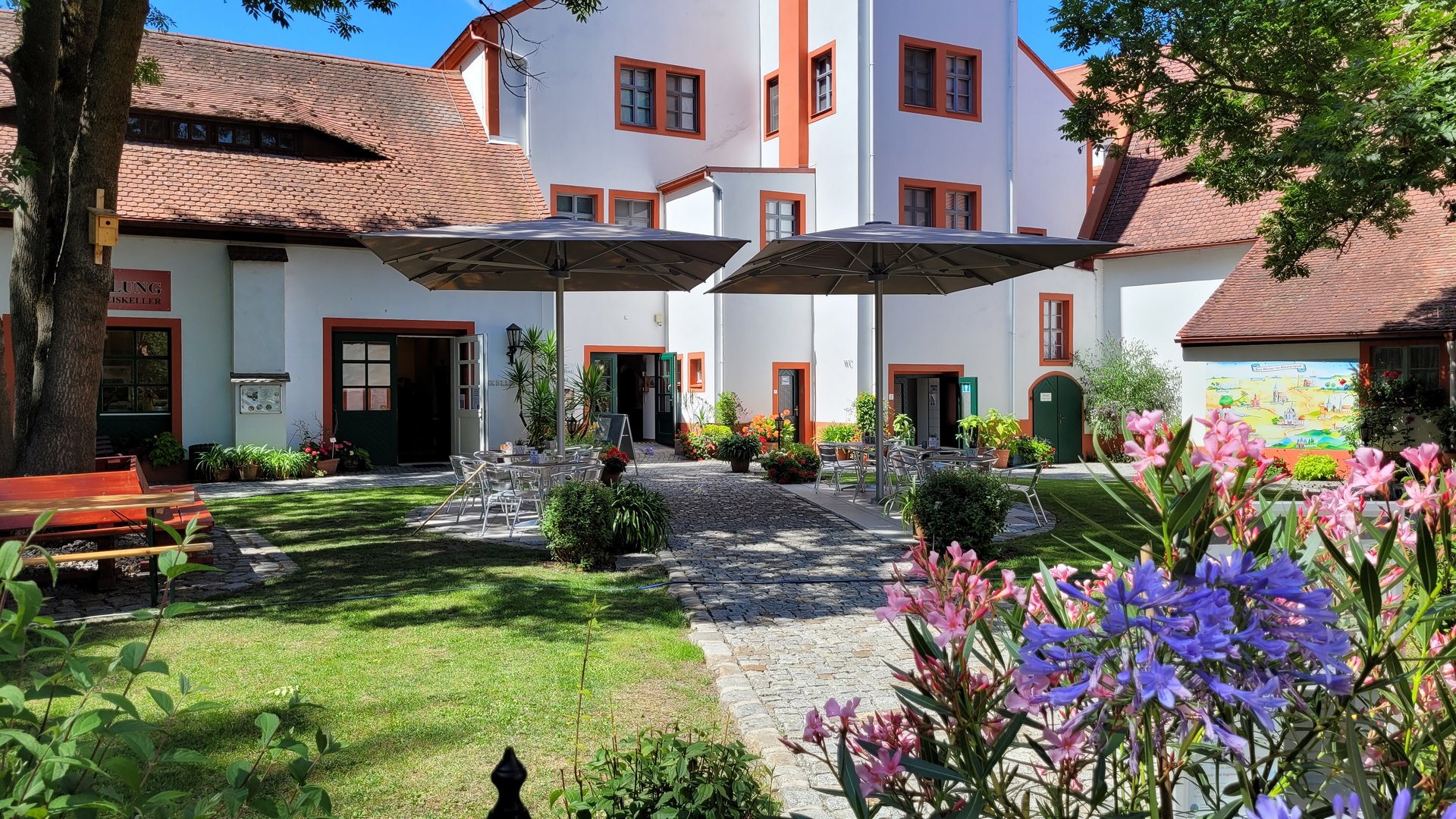 Blick auf einen Garten mit blühenden Pflanzen, im Hintergrund ein historisches Gebäude.