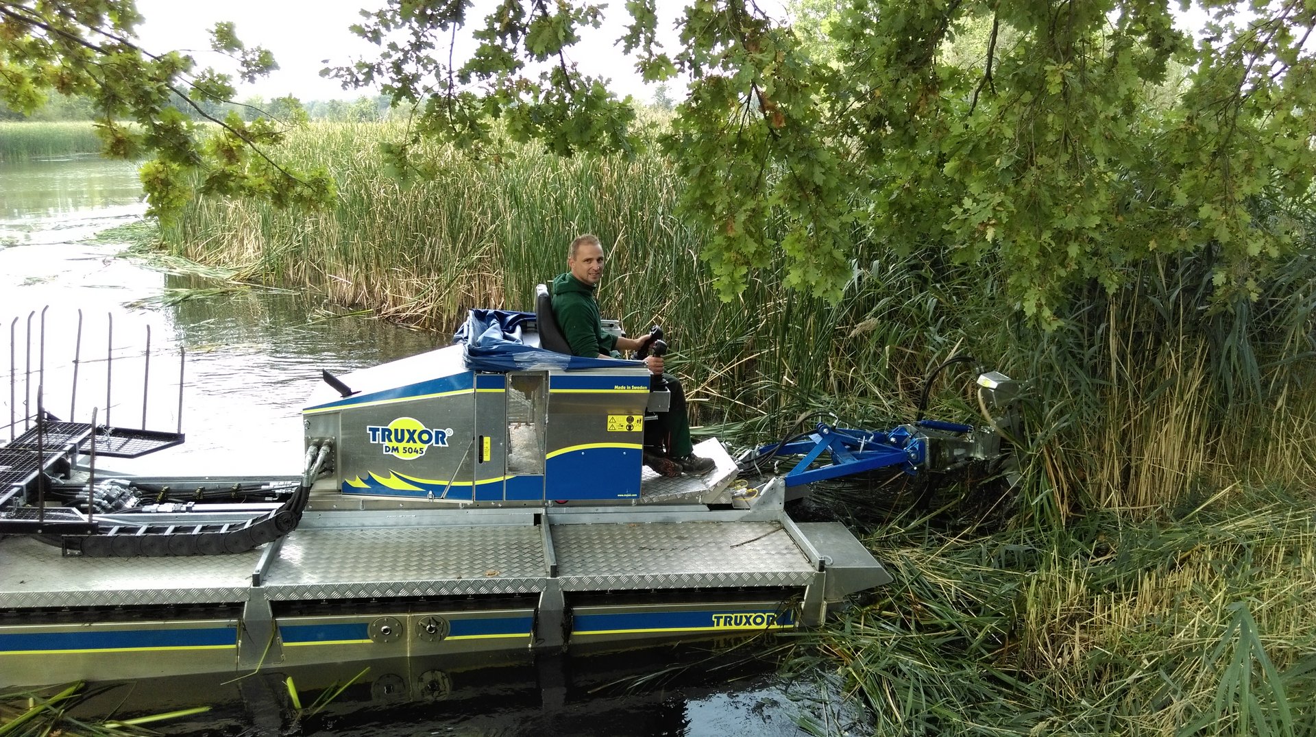 Ein Mann sitzt auf einer schwimmenden Schilfschneidemaschine in einem Teich.
